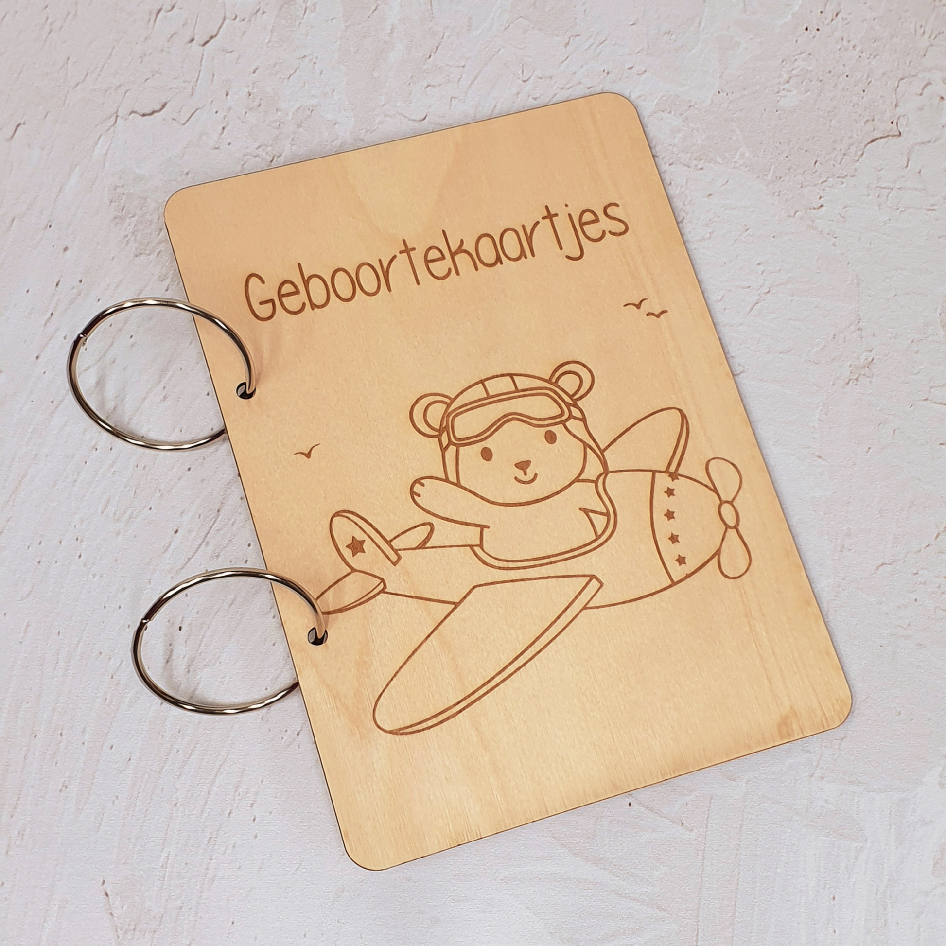 Bewaarbundel geboortekaartjes van hout met gegraveerde beer in vliegtuig